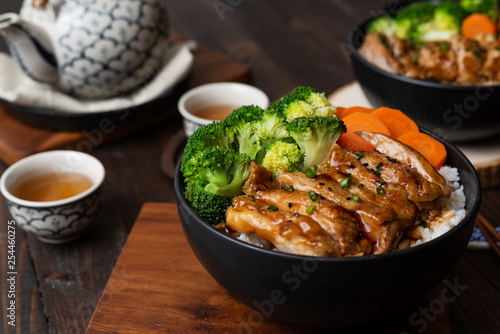 Japanese Food Style : Top view of Homemade Chicken Teriyaki grilled with rice , carrot , broccoli put on the black bowl and place on wooden table