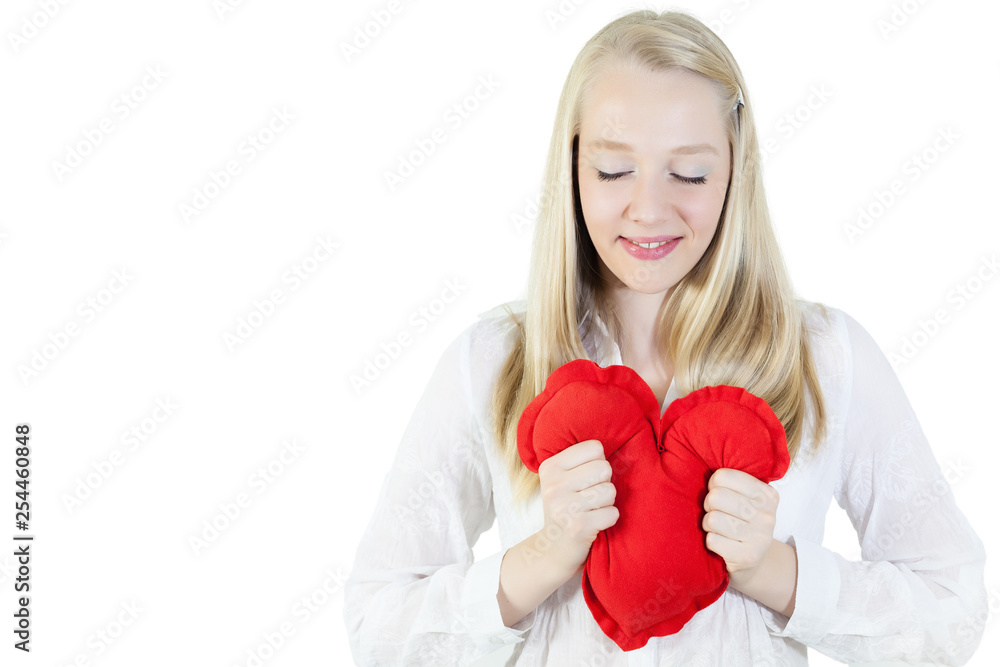 Young, blonde woman holding a heart shape pillow on a chest. Isolated, copy space