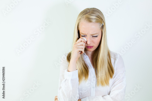 Sad, young, blonde woman holding tissue, looking down.
