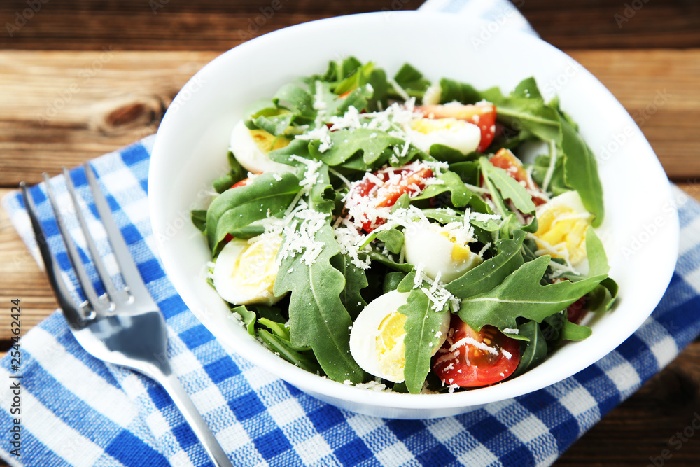 Salad with arugula leafs, tomatoes, eggs and fork on brown wooden table Salad with arugula leafs, tomatoes, eggs and fork on brown wooden table