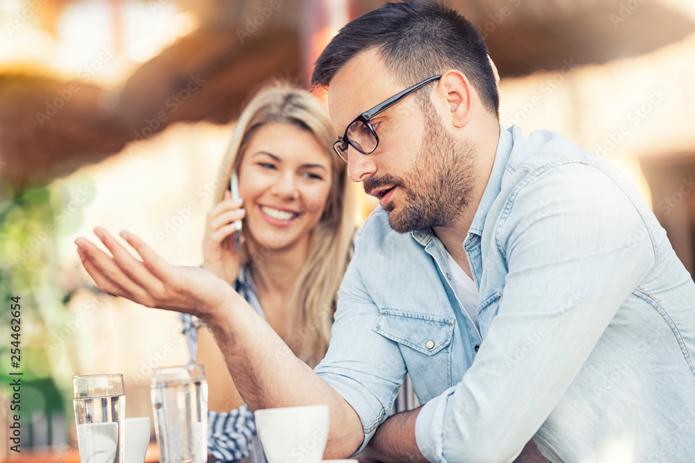Young unhappy man and his girlfriend who uses the phone Young unhappy man and his girlfriend who uses the phone