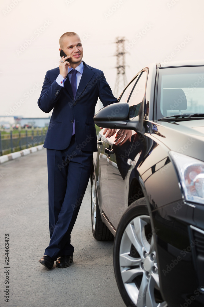 Young businessman in dark blue suit calling on cell phone next to his car Young businessman in dark blue suit calling on cell phone next to his car