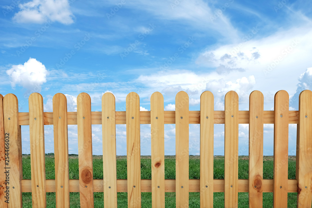 Beautiful wooden fence, green fields and blue sky background