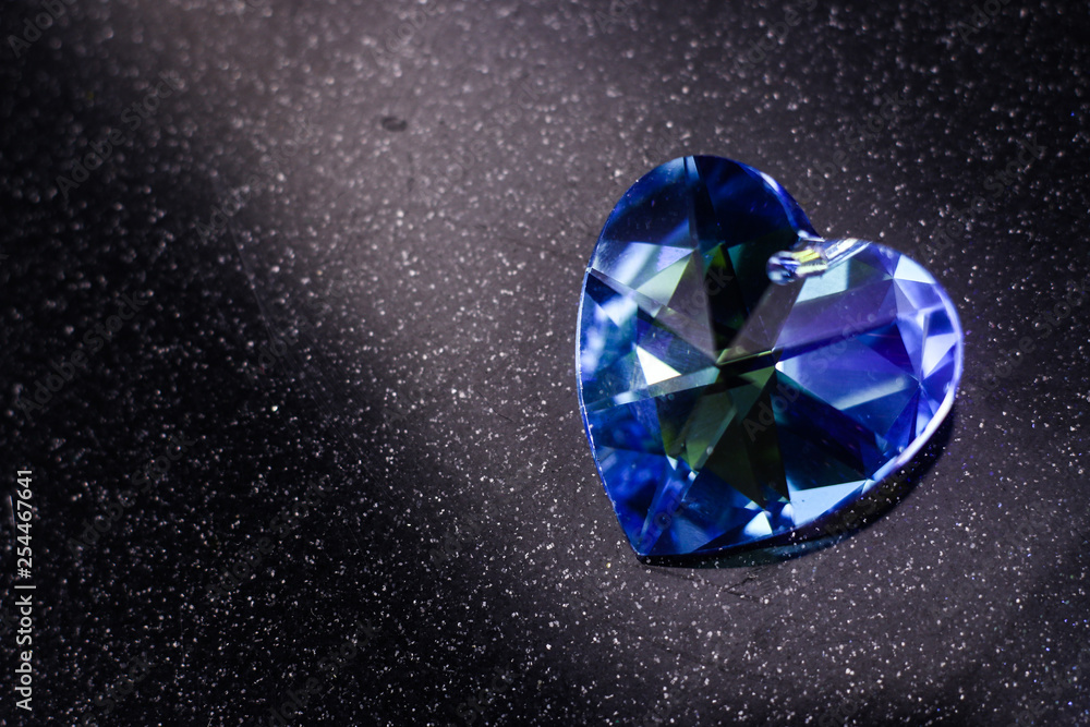 Blue heart-shaped facet crystal on the dark face background. The heart-shaped crystal with flashing facets Blue heart-shaped facet crystal on the dark face background. The heart-shaped crystal with flashing facets
