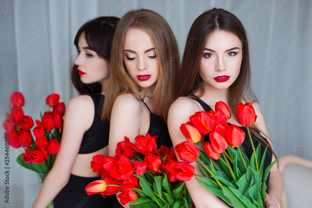 Fototapeta Fashion models in tender black dresses posing in sensual way at luxury interior full of tulips. Young woman sensuality.