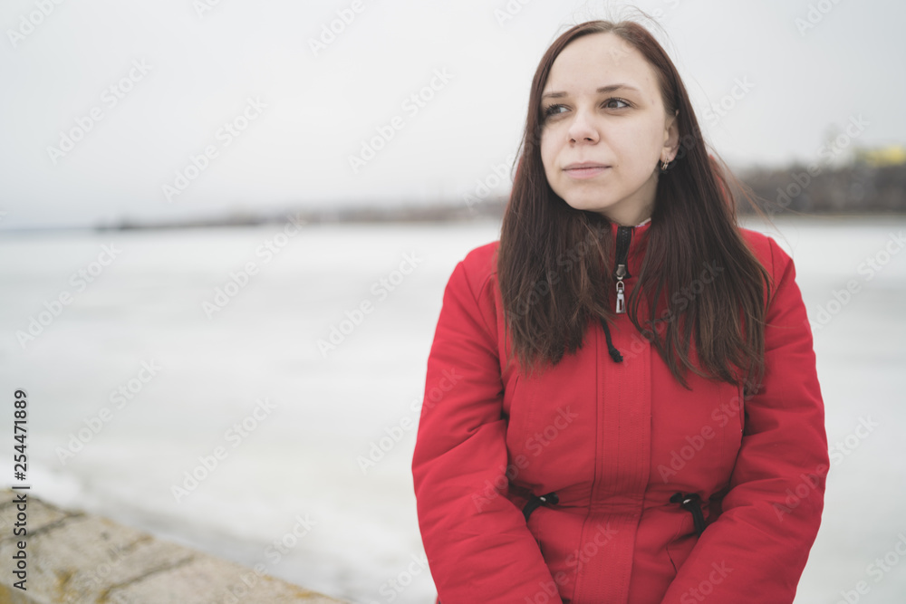 Beautiful girl in a red jacket on the pier in the spring posing against the water. Woman on the waterfront Beautiful girl in a red jacket on the pier in the spring posing against the water. Woman on the waterfront