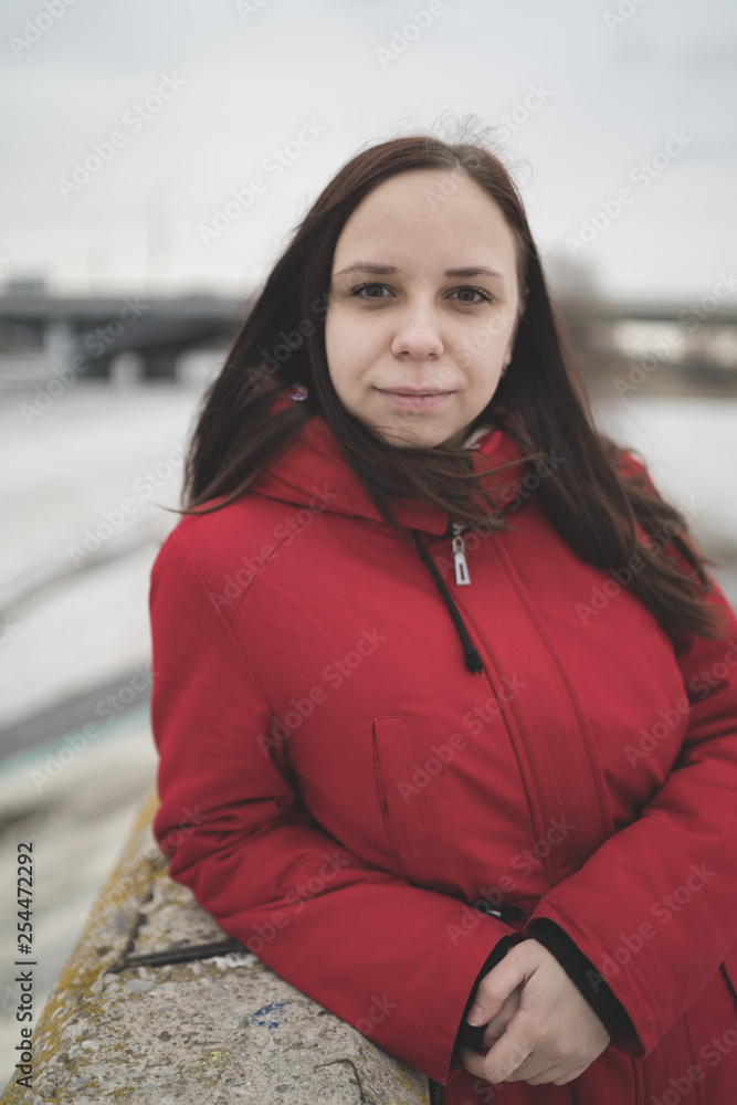 Beautiful girl in a red jacket on the pier in the spring posing against the water. Woman on the waterfront Beautiful girl in a red jacket on the pier in the spring posing against the water. Woman on the waterfront