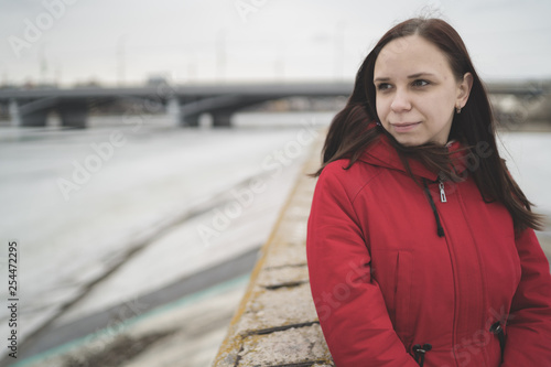 Beautiful girl in a red jacket on the pier in the spring posing against the water. Woman on the waterfront © Anton Dios