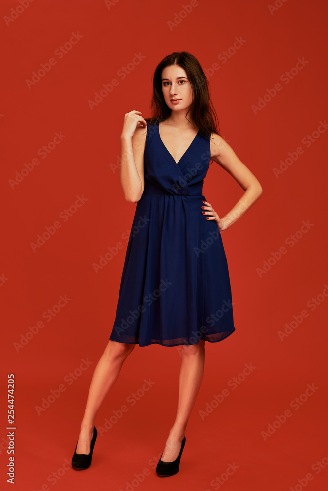 Beautiful young brunette woman in elegant blue cocktail dress and black high heels is posing for the camera