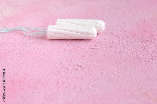 Two white cotton tampons with selective focus for monthly women’s menstrual days. Clean hygiene absorbent tampon on pink textured plaster background. Protect care products for menstruation period day 