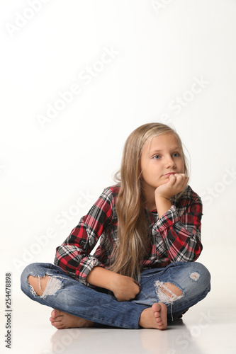 Girl with long blond hair sits on the floor. White background