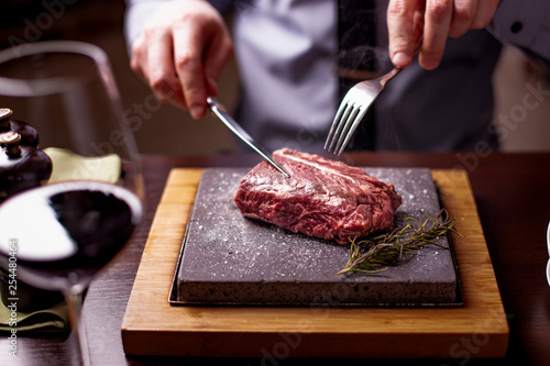 sirloin steak on a very hot stone being cooked by a man to his own taste on a wooden table with a knife and fork