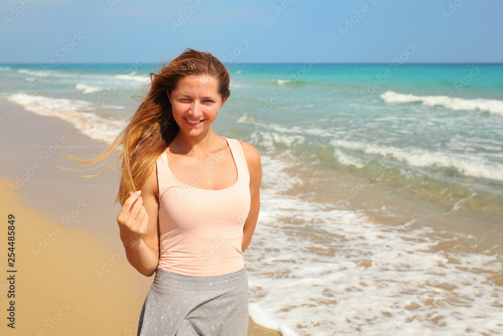 Young woman squinting one eye, as strong sun shines on her at the beach, sea in background. Young woman squinting one eye, as strong sun shines on her at the beach, sea in background.