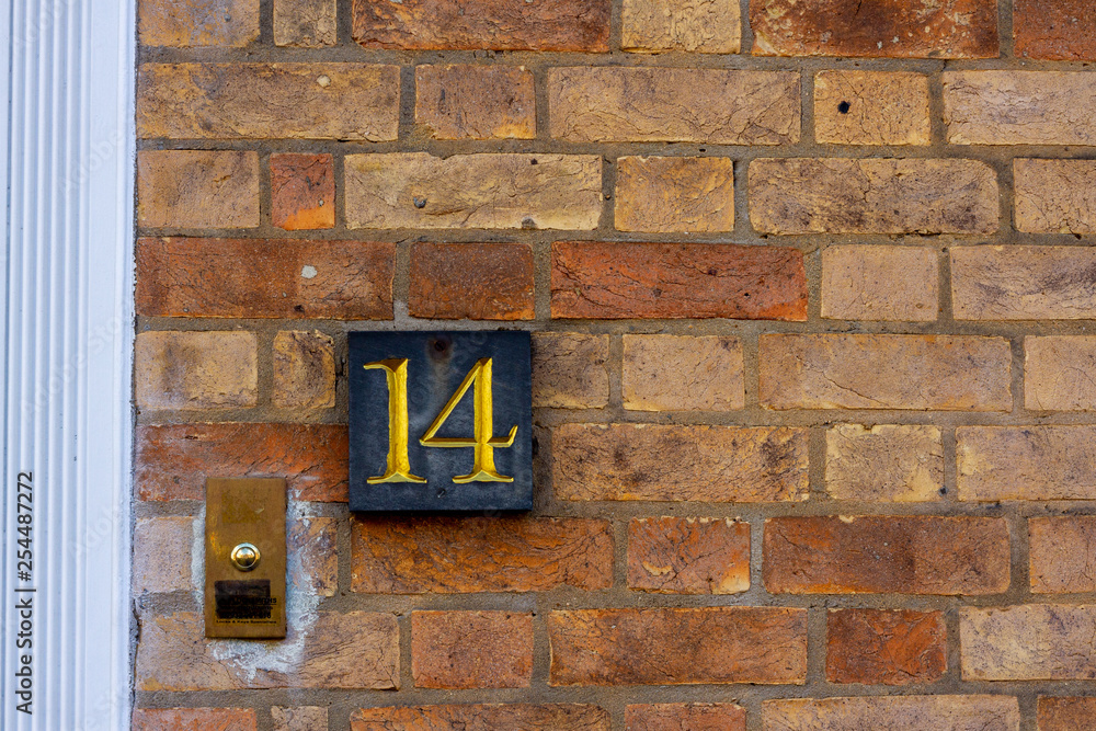 House number fourteen in gold on a black slate on a red brick wall with door bell outside a house. Fourteen is elegant House number fourteen in gold on a black slate on a red brick wall with door bell outside a house. Fourteen is elegant