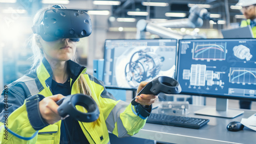Factory: Female Industrial Engineer Wearing Virtual Reality Headset and Holding Controllers, She Uses VR technology for Industrial Design, Development and Prototyping in CAD Software. photo