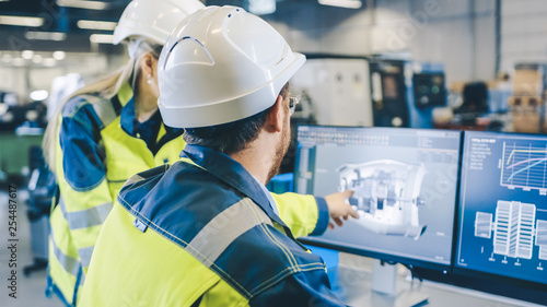 At the Factory: Male Mechanical Engineer and Female Chief Engineer Work Together on the Personal Computer, They Discuss Details of the 3D Engine Model Design. photo