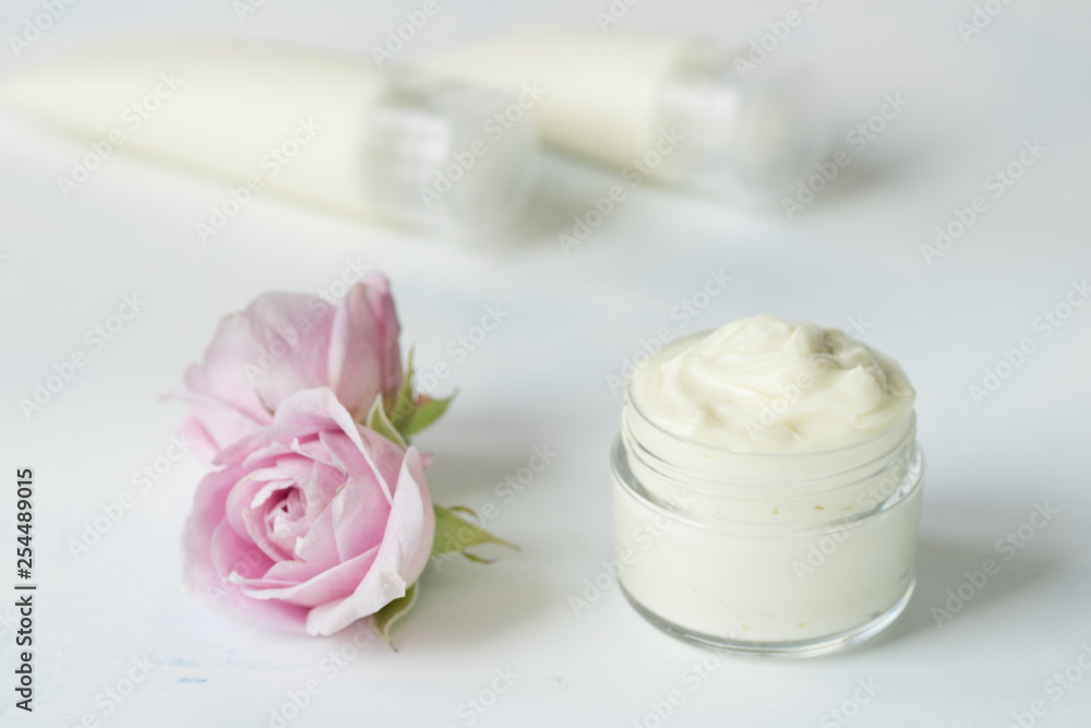 Natural face and body cream in a jar with a rose flower next to on a white background Natural face and body cream in a jar with a rose flower next to on a white background