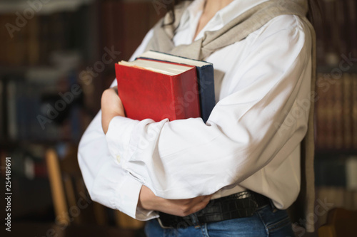 Croped photo of student girl holding books while standing at the library