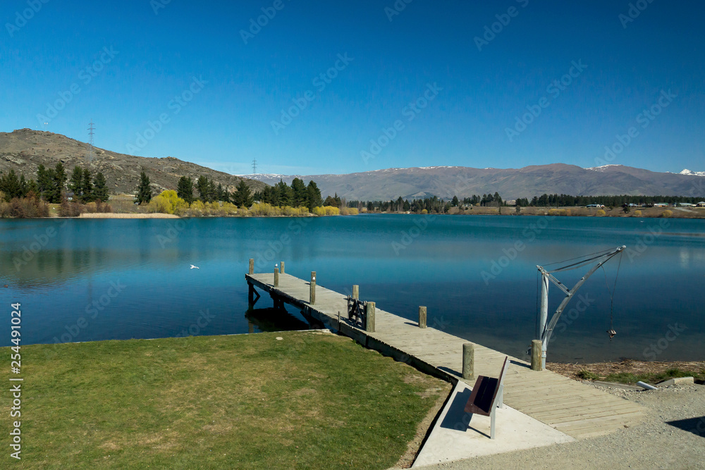 Wooden jetty on the Dunstan lake with snowy mountains on the background in Cromwell in New Zealand.