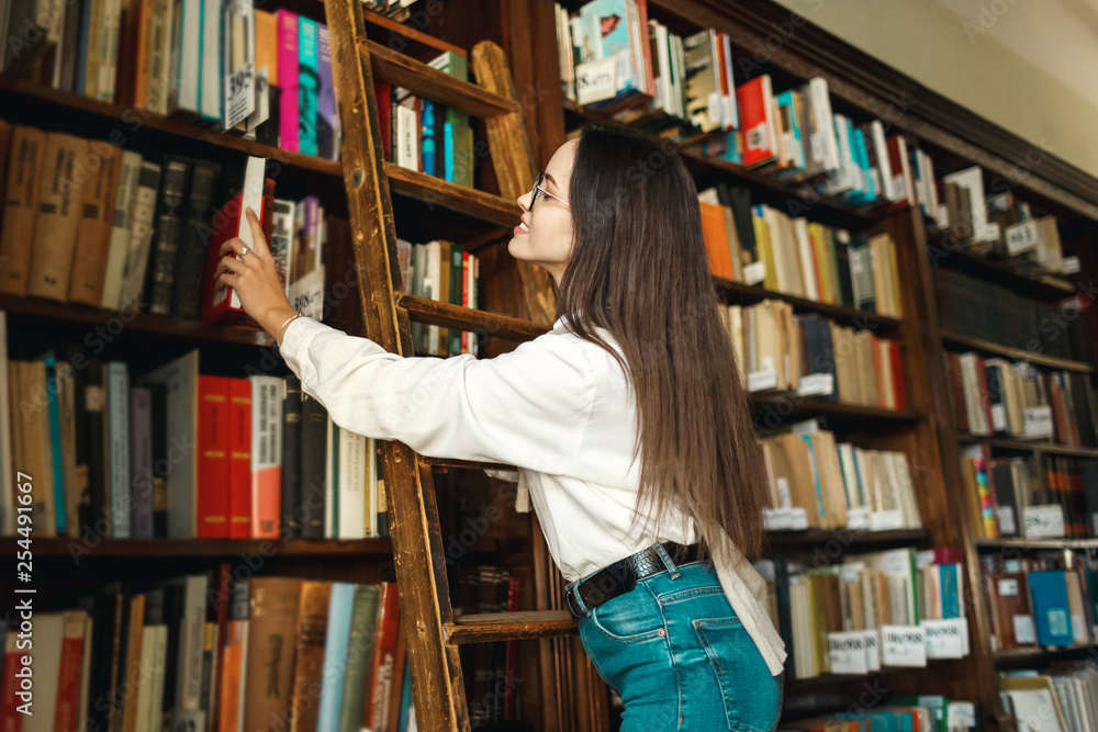 College girl takes out a book from the shelves at the library College girl takes out a book from the shelves at the library