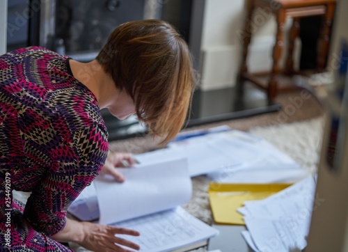 A young woman, working at home, kneels on the floor collating papers.