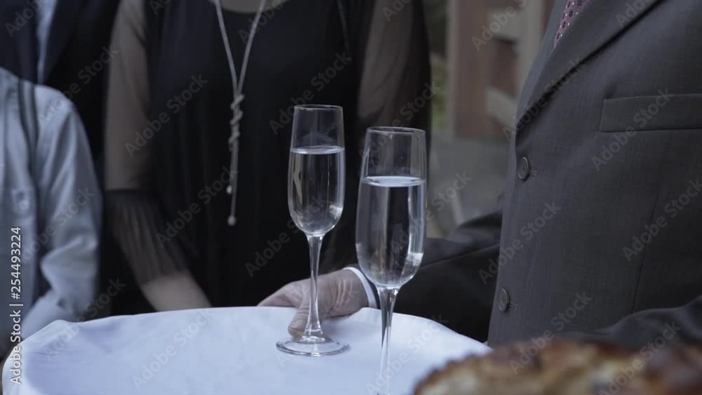 Elderly man holding champagne glasses on a tray.
