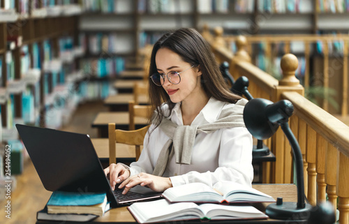 Pretty female student with laptop and books working in a high school library