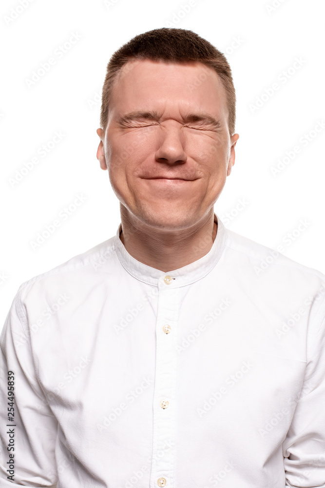 Charming handsome young man in a white shirt is making faces, while standing isolated on a white background Charming handsome young man in a white shirt is making faces, while standing isolated on a white background