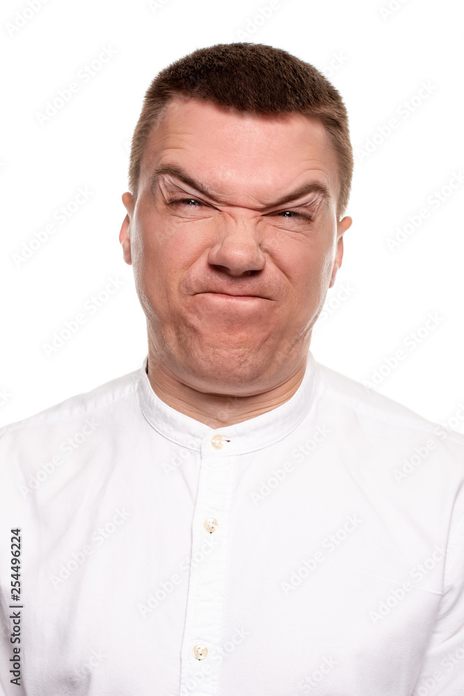Charming handsome young man in a white shirt is making faces, while standing isolated on a white background Charming handsome young man in a white shirt is making faces, while standing isolated on a white background