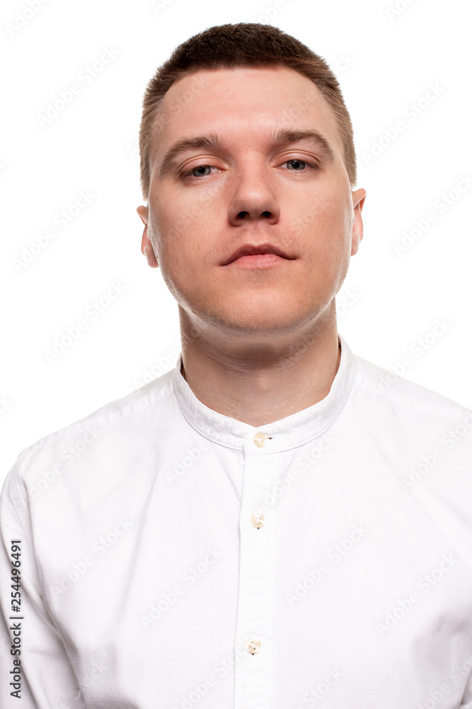 Obraz premium Charming handsome young man in a white shirt is making faces, while standing isolated on a white background