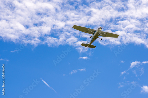 Single engine sport airplane in the air in front of clouds, condensation stripes of a jet in the background