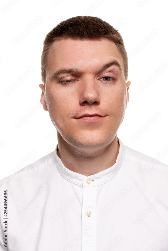 Charming handsome young man in a white shirt is making faces, while standing isolated on a white background Charming handsome young man in a white shirt is making faces, while standing isolated on a white background