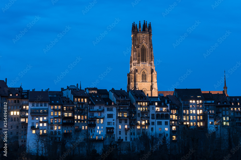 Twilight over the Fribourg old town and the illuminated Cathedral Saint Nicolas in Switzerland. Fribourg is one of the best preserved medieval old town in the country.
