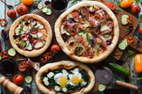 Freshly made yummy pizza party. Flatlay of puffy pizzas with pancetta, aubergines, spinach, eggs, bell pepper and arugula served with raw vegetables and herbs on oak boards