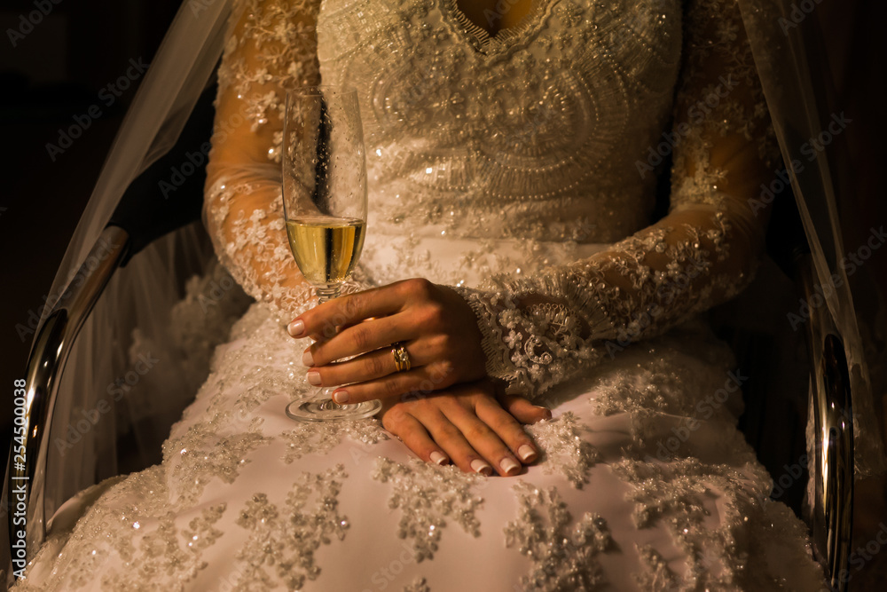 Noiva com seu vestido de casamento, segurando uma taça de espumante de forma delicada e com anéis nas mãos Noiva com seu vestido de casamento, segurando uma taça de espumante de forma delicada e com anéis nas mãos