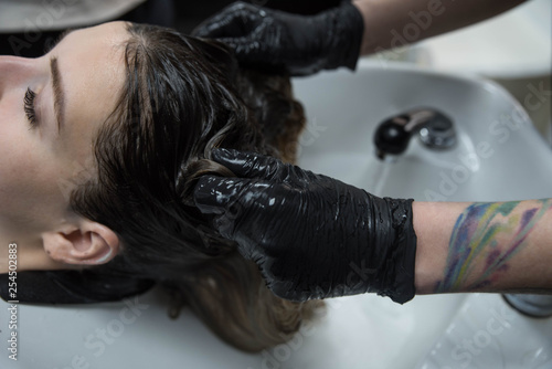 Beauty concept - Professional hairdresser applying shampoo, washes color paint off and massaging hair of a customer. Woman having her hair washed in a hairdressing beauty salon