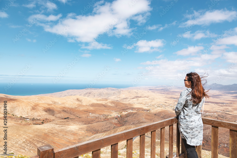 Woman looking at volcanic mountains and ocean landscape from Mirador de Morro Velosa viewpoint, Fuerteventura, Canary Islands, Spain