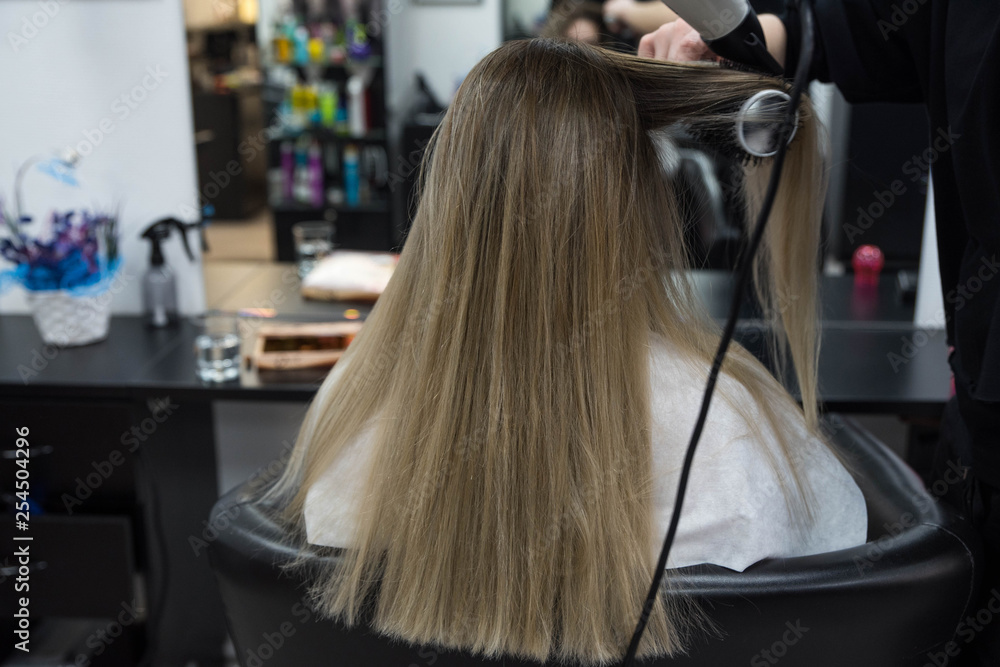 Professional hairdresser brushing beautiful client’s hair with round brush