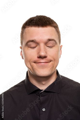 Handsome young man in a black shirt is making faces, while standing isolated on a white background