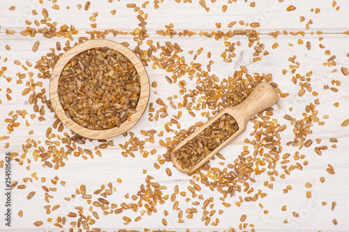 Lot of whole raw bulgur grains in a scoop with wooden bowl flatlay on white wood photo