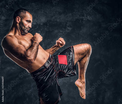 Professional Muay Thai boxer showing kick fighting technique. Studio photo against a dark textured wall