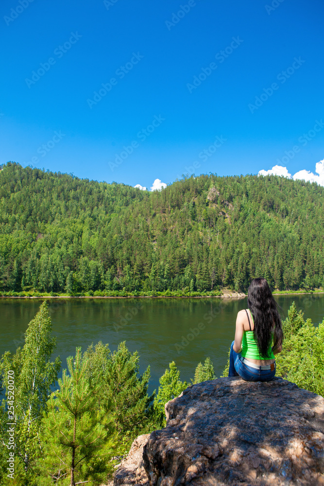 Young traveling woman sitting on the top of the mountain cliff.