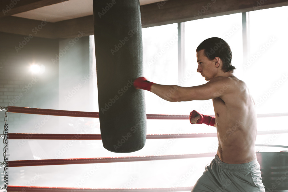 angry boxer standing in boxing pose near punching bag on black with smoke