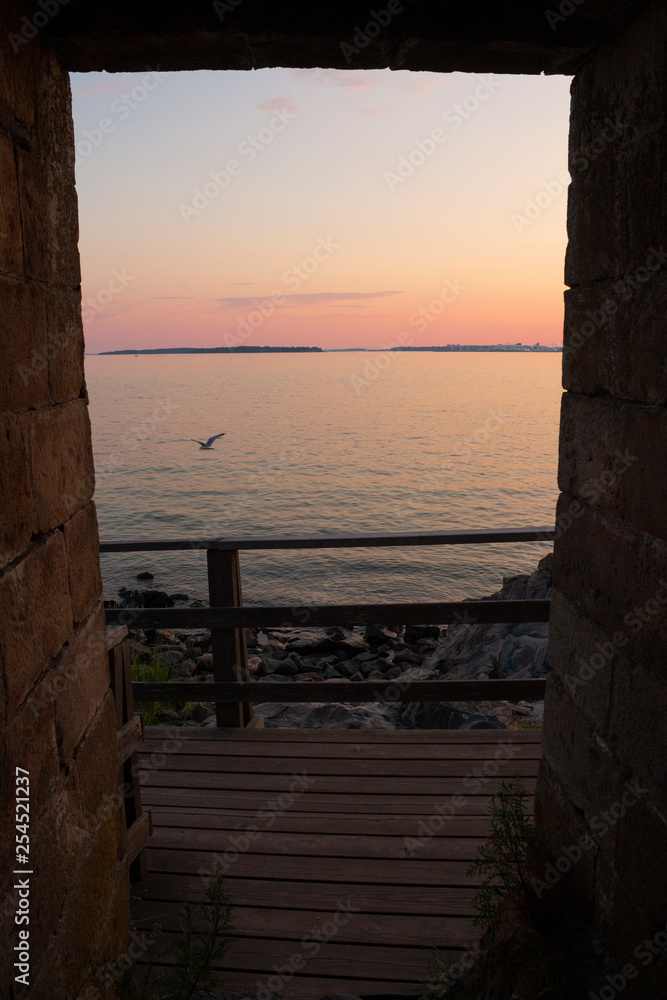 Doorway and walkway in the old brick wall of the historic fort fort on Suomenlinna island Sveaborg and view of the Gulf of Finland in the evening of a summer day.