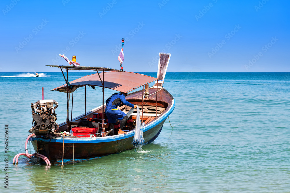 Fisherman on a motor wooden boat pull fishing nets. Sunny day, blue sky and sea.