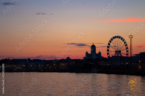 View of the embankment of Helsinki, the Ferris wheel, lights and the silhouette of the Cathedral of St. Nicholas from the Gulf of Finland at dusk on a bright summer night in the capital of Finland.