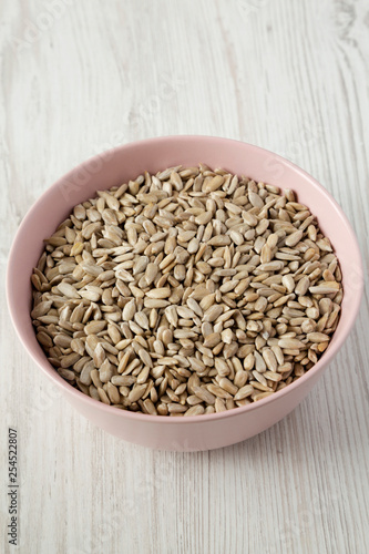 Dry hulled sunflower seeds in a pink bowl over white wooden background, low angle view. Closeup.