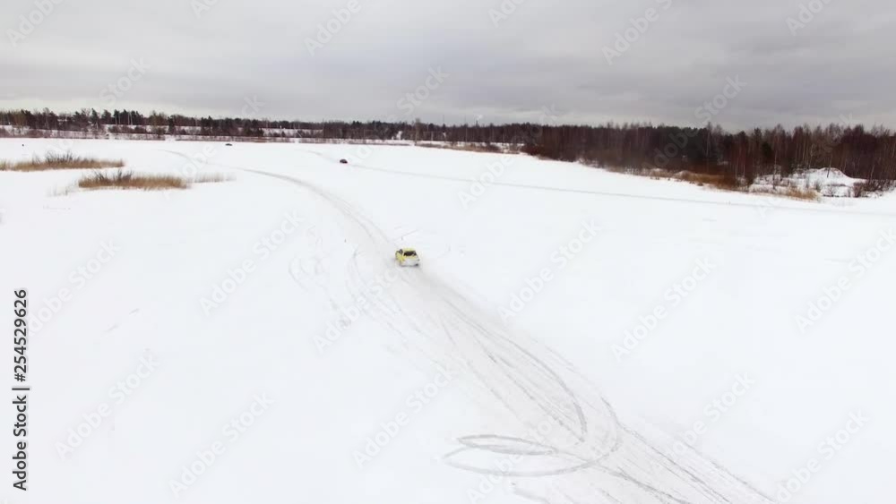 Car drives by icy track on snow covered lake at winter. Aerial view. Sport car racing on snow race track in winter. Driving a race car on a snowy road Car drives by icy track on snow covered lake at winter. Aerial view. Sport car racing on snow race track in winter. Driving a race car on a snowy road