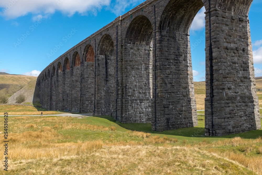 The sweeping majestic Ribblehead Viaduct stands tall above the Ribble Valley, Yorkshire, England carrying the Settle to Carlise railway against a bright blue sky
