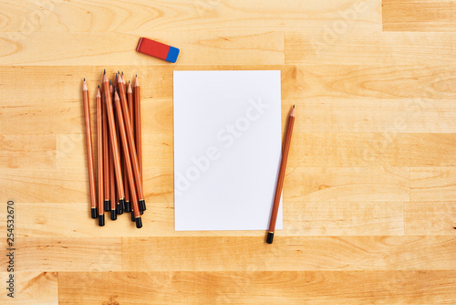 Top view of wooden office desk with blank sheet of paper, eraser and a bunch of pencils. Flat lay. Copy space for text or design.